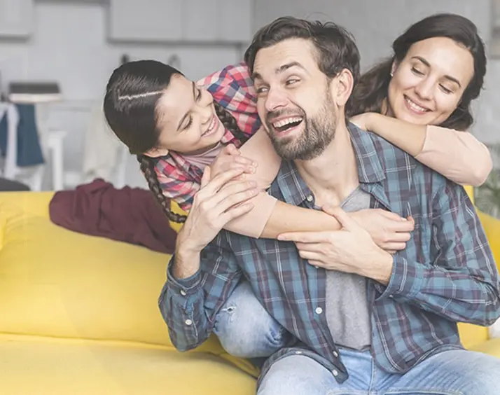 Padre, madre e hija abrazados y riendo en el sillón de su casa